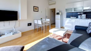 Een moderne woonkamer met een flatscreen televisie, een bank, een salontafel en een eethoek met een witte tafel en stoelen.