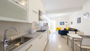 Een moderne keuken met een roestvrijstalen spoelbak, witte kasten en een eethoek met een tafel en stoelen.