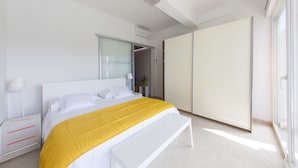 Een moderne slaapkamer met een groot bed, een nachtkastje, een bankje, een garderobe en een schuifdeur.