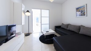 Een moderne woonkamer met een flatscreen televisie, een witte salontafel, een zwarte bank en een zwart tapijt.