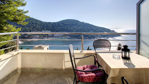 Een balkon met een tafel, stoelen en uitzicht op zee en bergen.