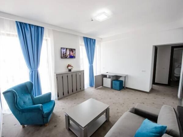 A modern living room with a sofa, a blue armchair, a coffee table, and a TV mounted on the wall. - La mer Mamaia Nord (Navodari)