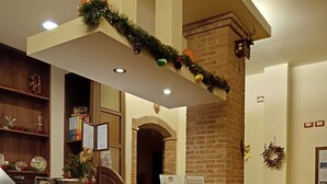 A reception area with a brick counter, a small table with a yellow tablecloth, and a decorative wreath on the wall. - B&B Villa Hirschen (Zafferana Etnea)