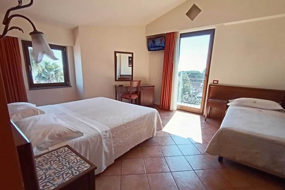 Habitación de hotel con dos camas, televisión, ventana con cortinas y balcón.