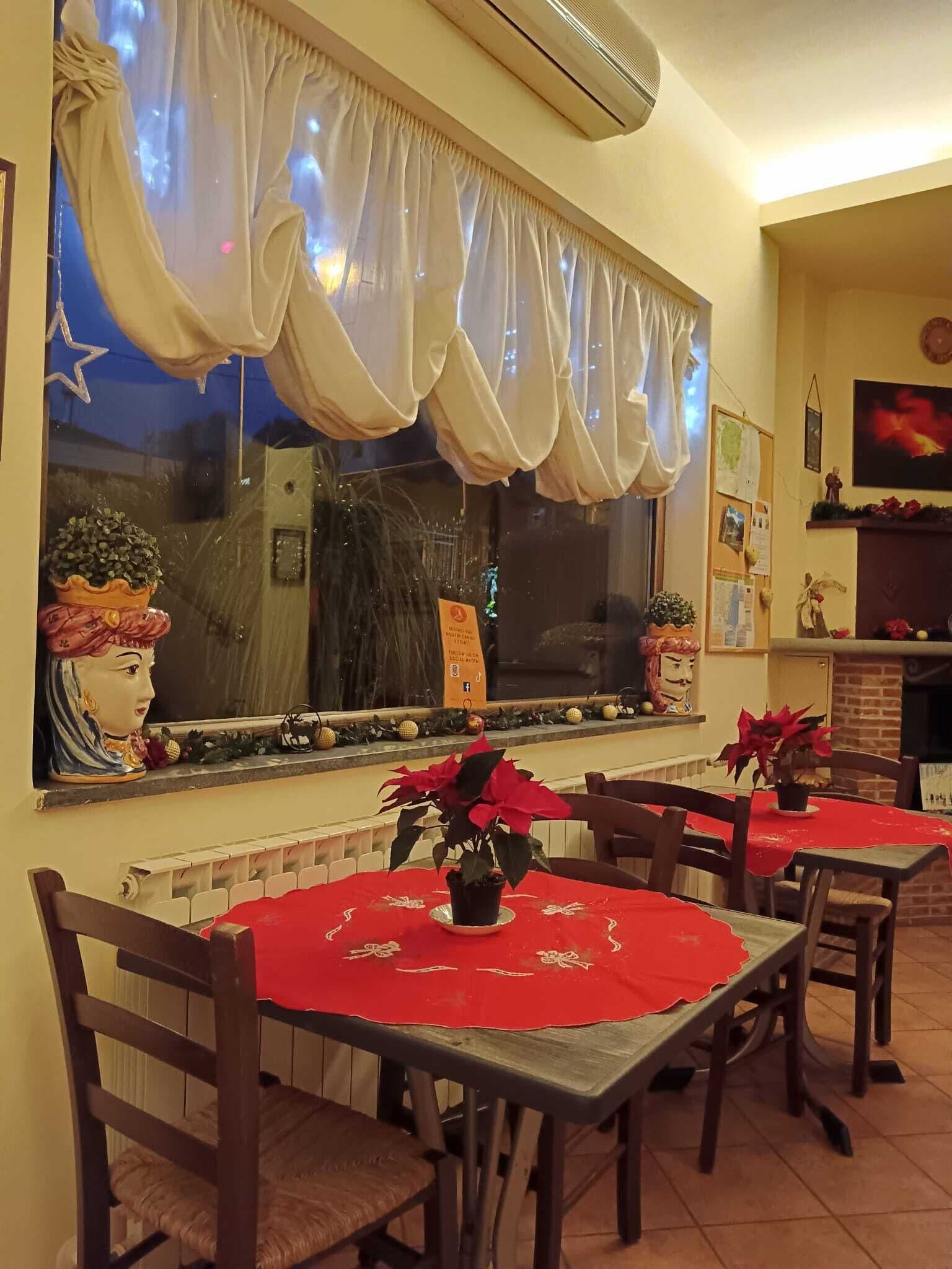 A restaurant with a large window, red tablecloths, and potted plants.