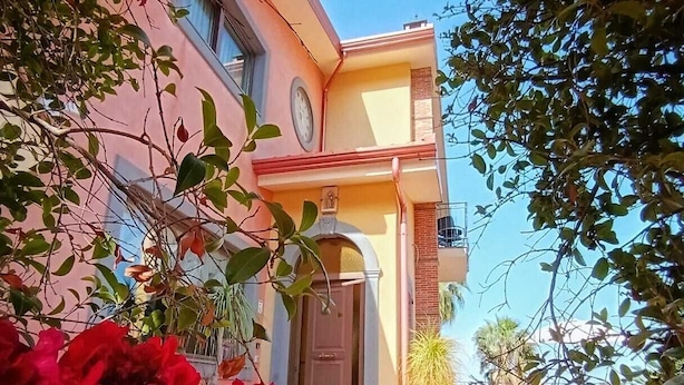 A two-story building with a balcony on the second floor, a door with a small window, and a clear blue sky in the background. - B&B Villa Hirschen (Zafferana Etnea)