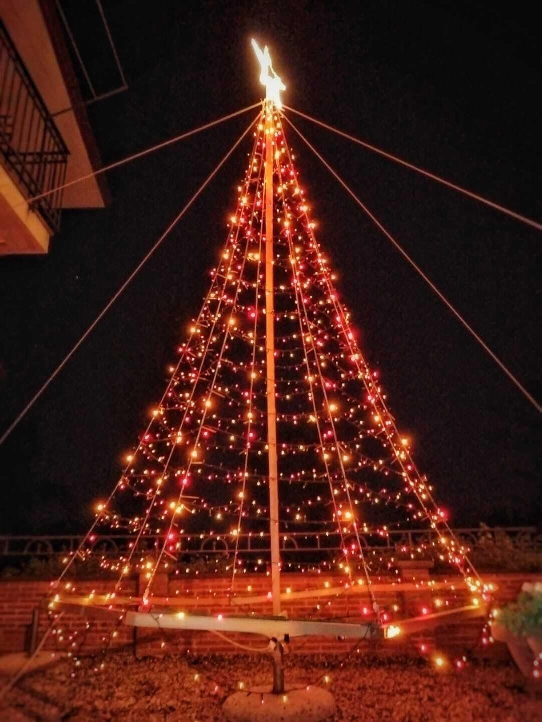 A large, illuminated triangular structure with a central pole and multiple strings of lights.