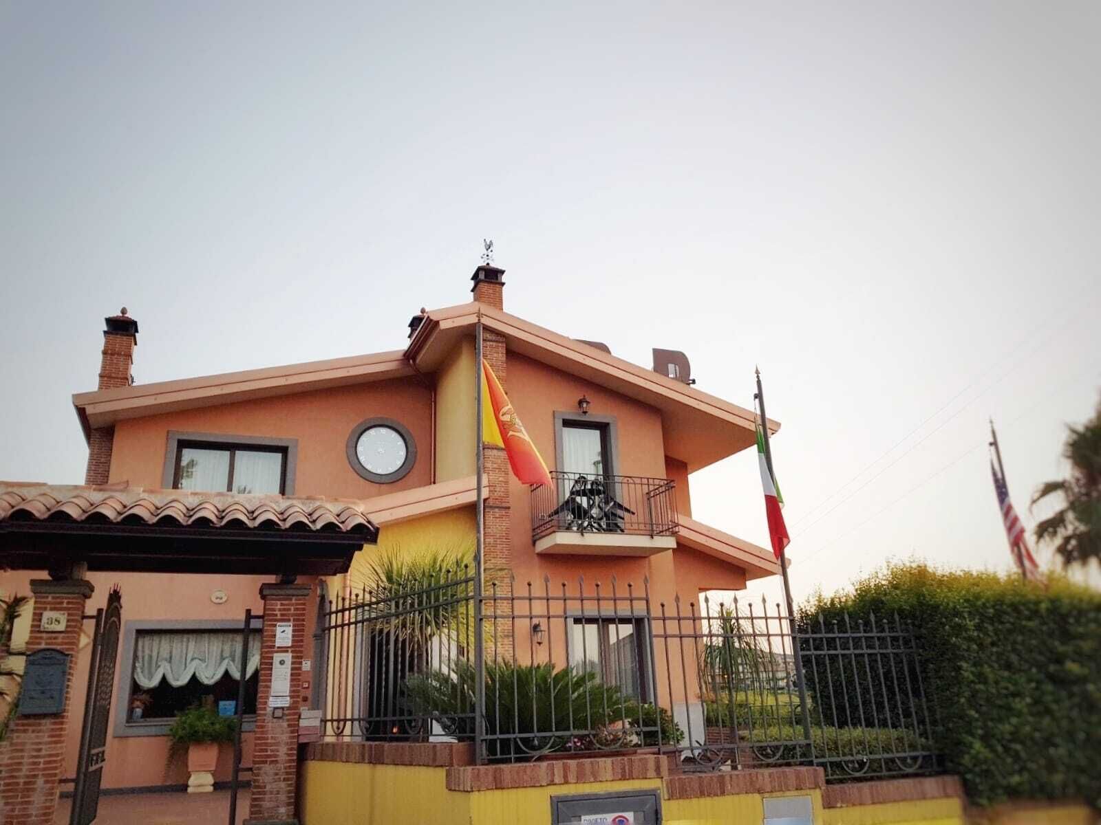 A two-story house with a balcony, a flag, and a gate.