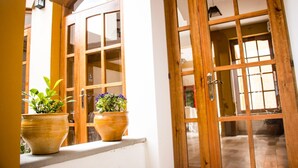 A doorway with wooden panels and glass panels, leading to an interior space. There are two potted plants on the ledge outside the doorway. - Hotel Suiza Peruana (Huaraz)