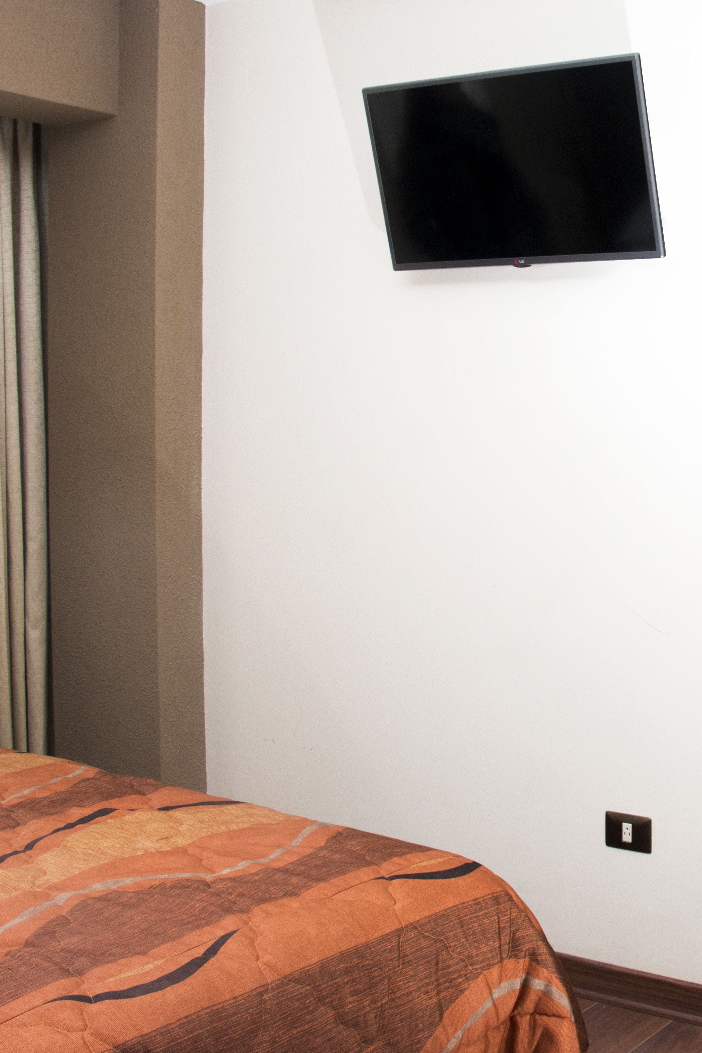 Habitación de hotel con cama, televisor de pantalla plana montado en la pared y un enchufe.