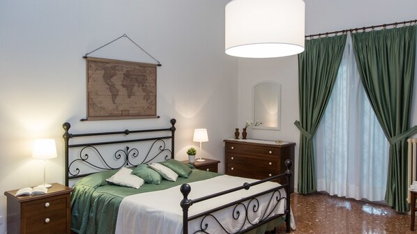 A bedroom with a bed, nightstands, a dresser, a map on the wall, a mirror, and green curtains.