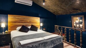 A bedroom with a wooden headboard, a bed with a grey blanket, a nightstand with a lamp, and a wooden railing.