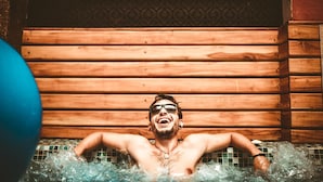 A person in a wooden cabin-style hot tub with tiled walls.