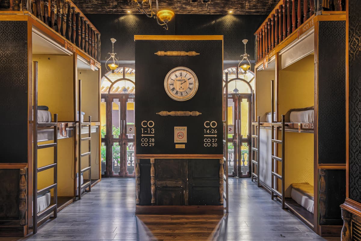 A hotel corridor with bunk beds, a large wall clock, and a sign indicating room numbers.