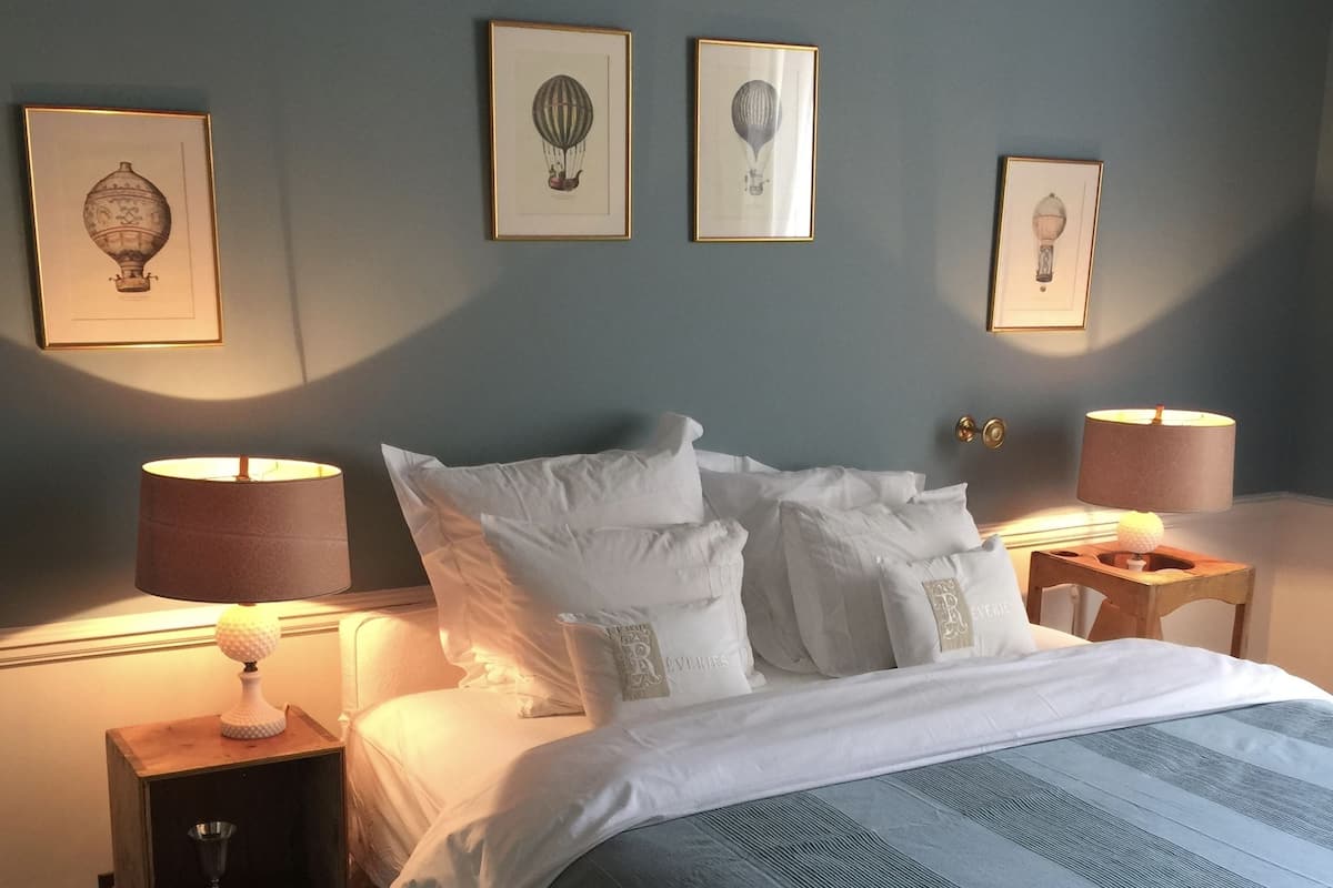 Una cama bien hecha con sábanas blancas y una colcha a rayas azules, dos lámparas de noche y cuadros en la pared.