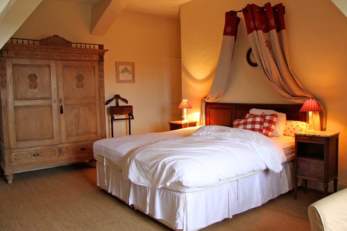 Un dormitorio con una cama grande, un armario de madera, una mesita de noche con lámpara y una cortina decorativa.