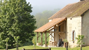 A rustic farmhouse with a wooden porch, a dining area, and a large tree in the foreground. - Château de Villette (Poil)