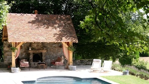 A stone building with a tiled roof, a pool, and outdoor seating. - Château de Villette (Poil)