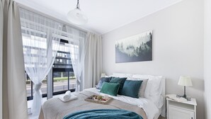A modern bedroom with a bed, bedside table, and a window with sheer curtains. - P&O Apartments Cybernetyki (Warsaw)