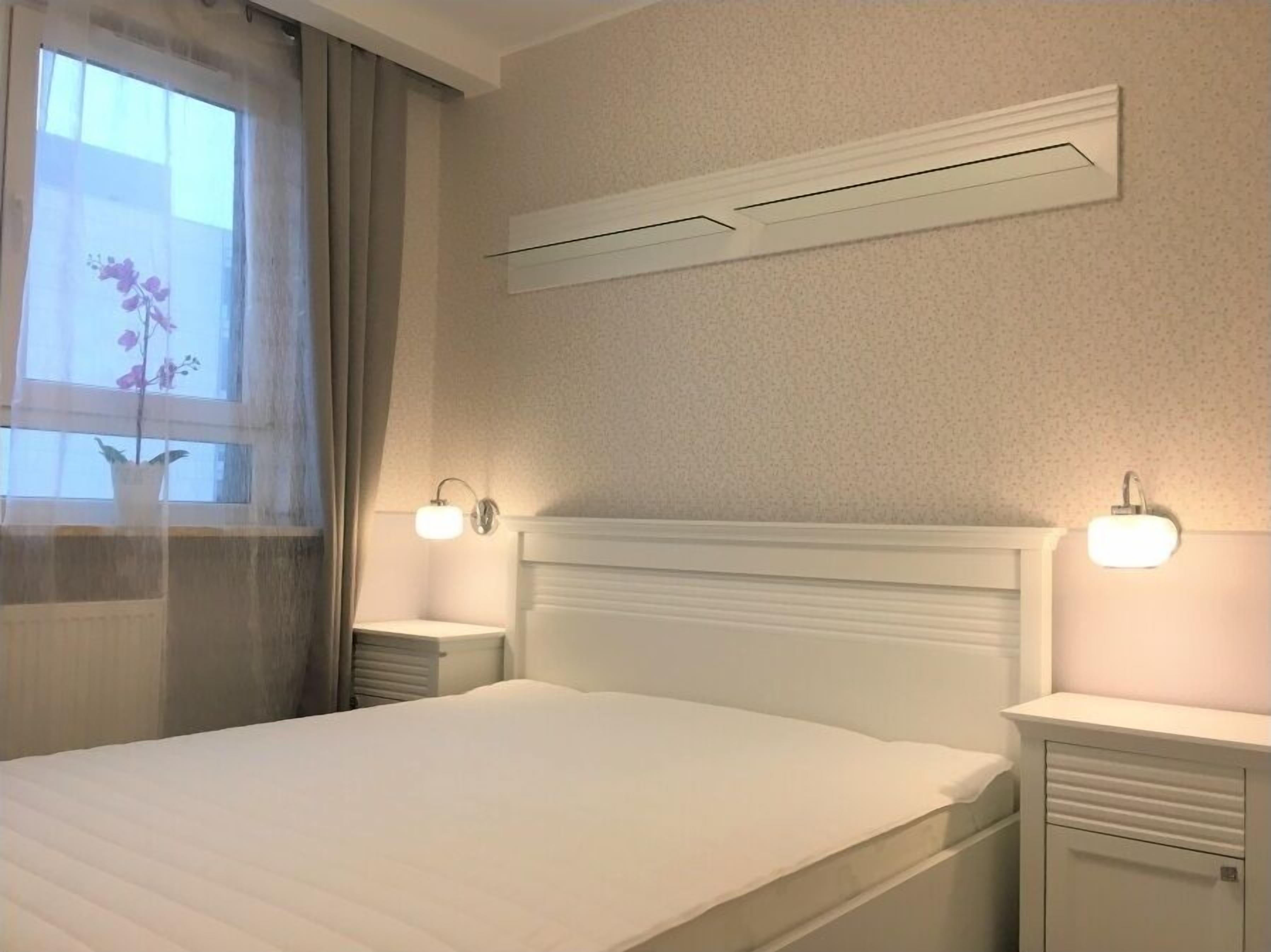 Ein Schlafzimmer mit einem Bett, zwei Nachttischen, einer Wand-Klimaanlage und einem fenster mit Vorhängen.