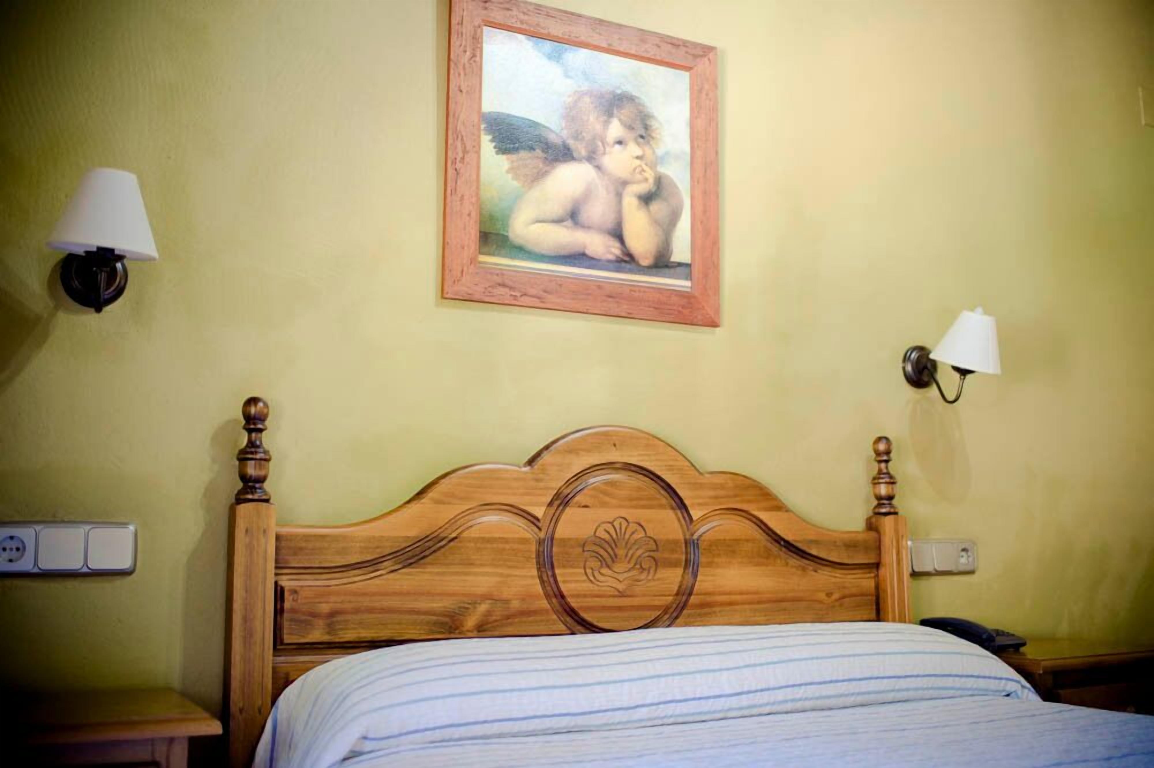 A bedroom with a wooden headboard, a framed picture on the wall, and two bedside lamps.