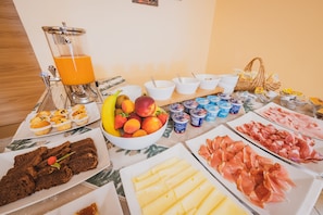 A breakfast buffet with various food items, including fruits, pastries, and meats.