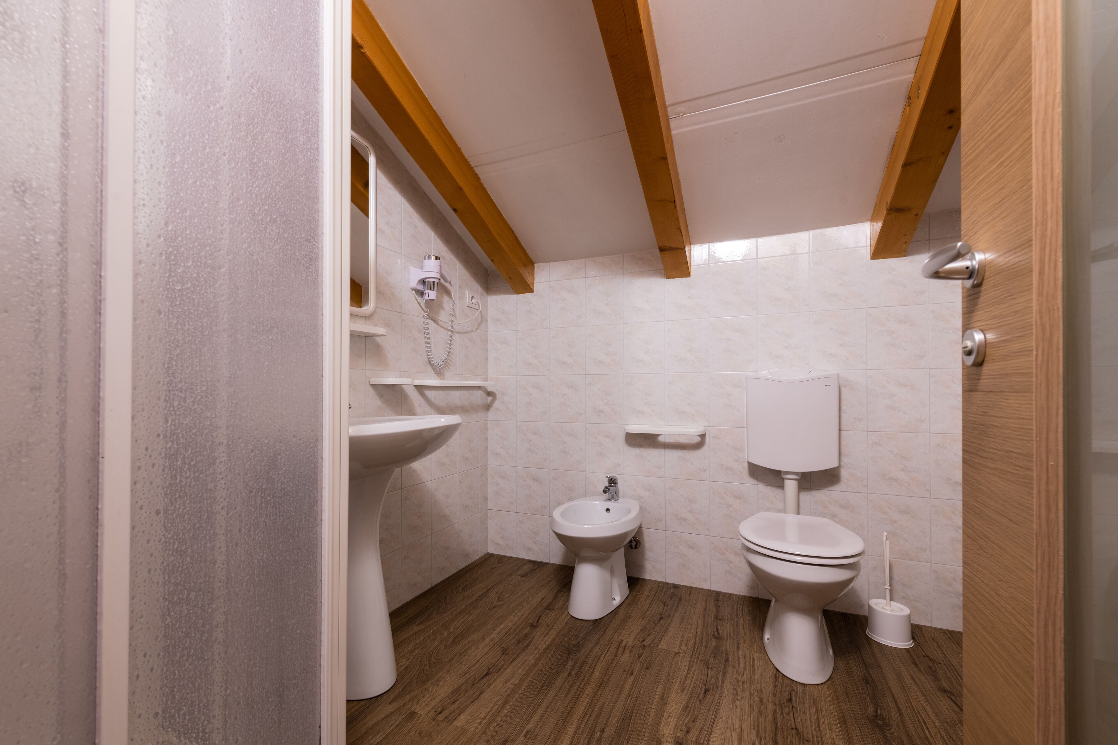 Ein kleines Badezimmer mit Holzboden, Waschbecken in Weiß, einem Bidet und einer Toilette.