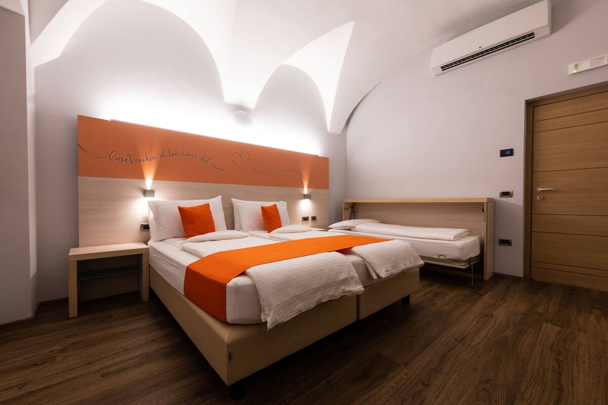 A modern hotel room with a large bed, a smaller bed, a nightstand, a wooden wardrobe, and a wall-mounted air conditioner.