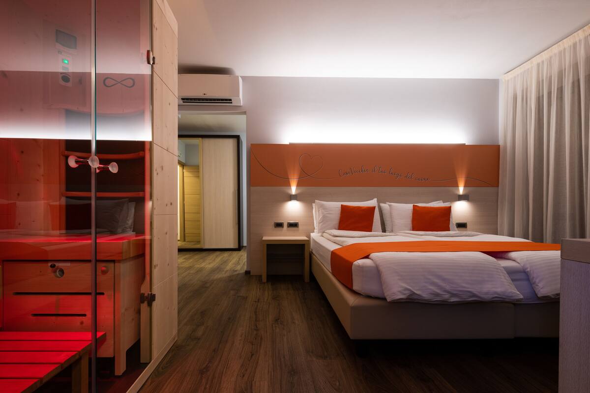A hotel room with a bed, bedside tables, a wardrobe, and a glass partition.