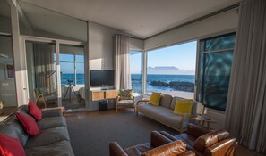 A spacious living room with a large window offering a view of the ocean and rocky coastline.