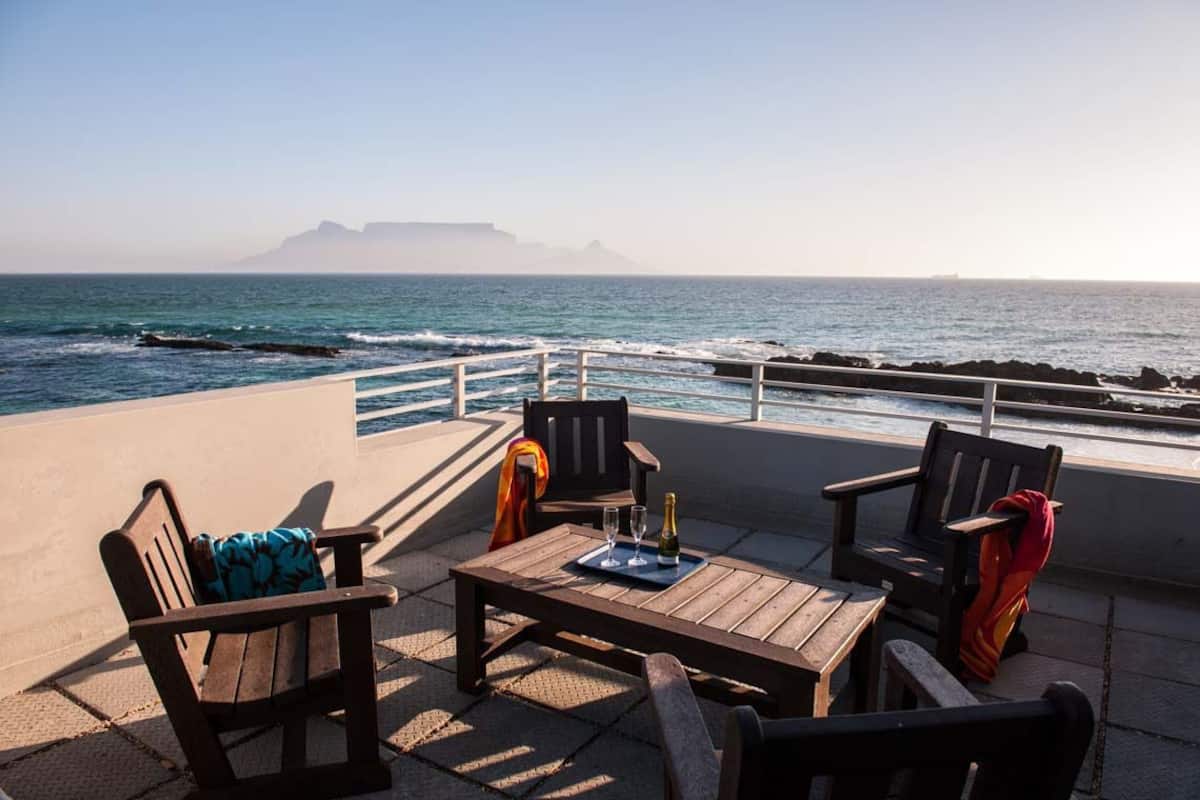 Une terrasse en bord de mer, dotée de mobilier en bois et d’une table, offrant une vue sur l’océan.