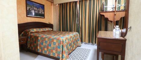 A hotel room with a bed, a bedside table, a dresser, a mirror, and a curtain.