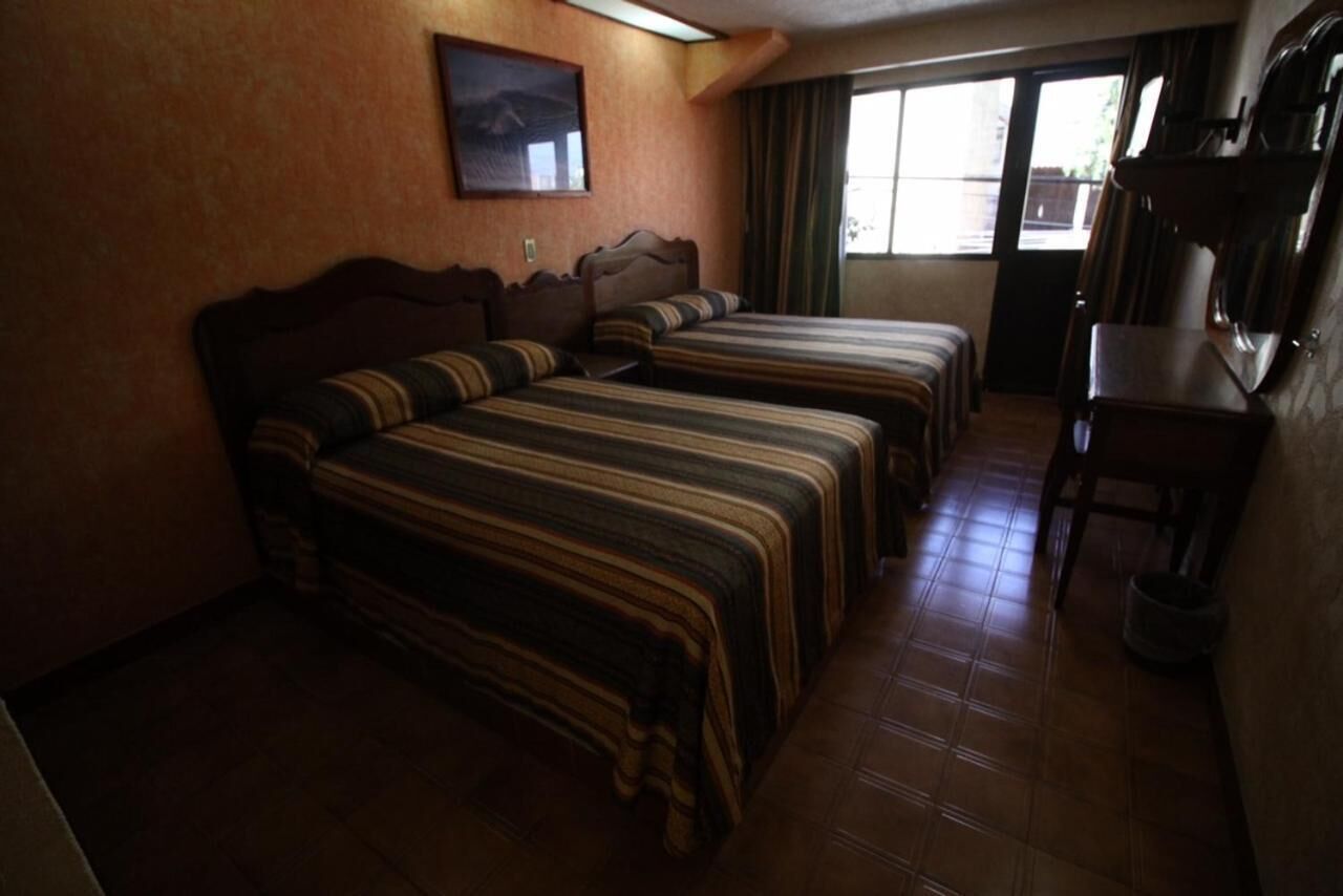 Een hotelkamer met drie bedden, een houten hoofdeinde, een inlijsting afbeelding aan de muur en een raam met gordijnen.