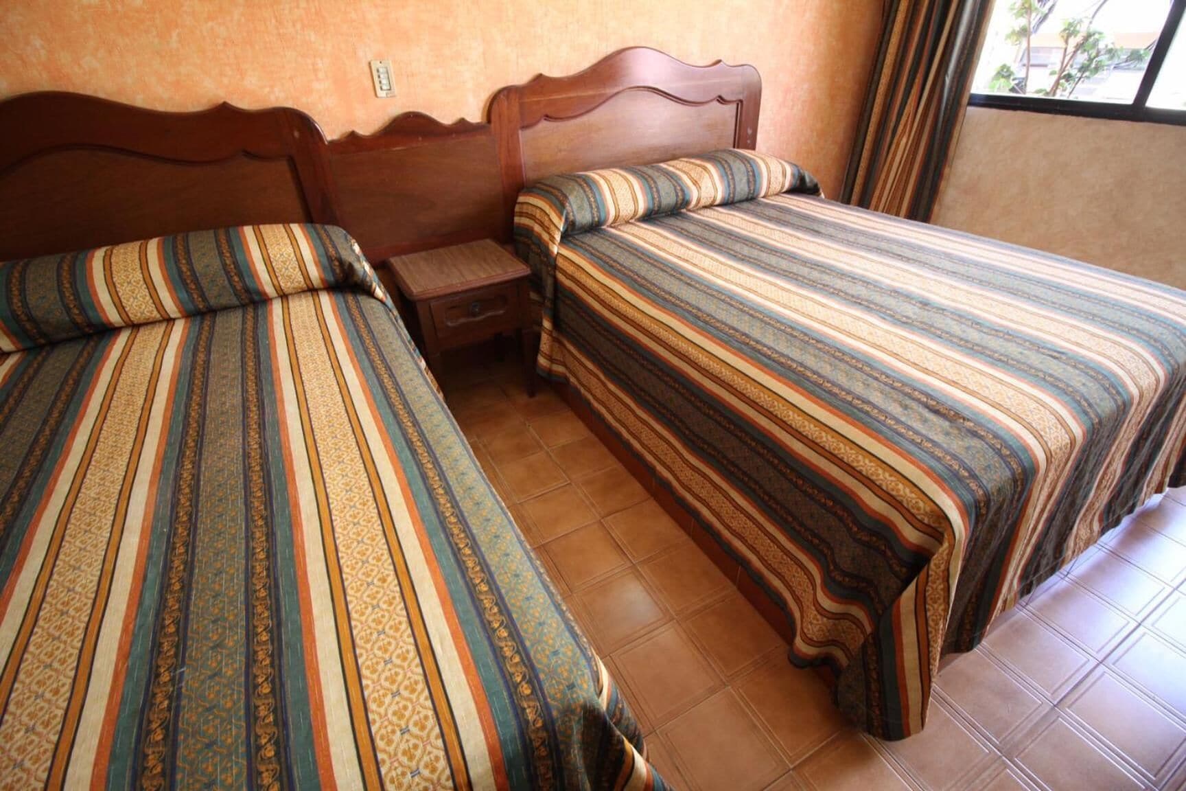 Ein Zimmer mit zwei Betten, jeweils mit gestreifter Bettwäsche, einem Holz-Kopfteil und einem kleinen Nachttisch.