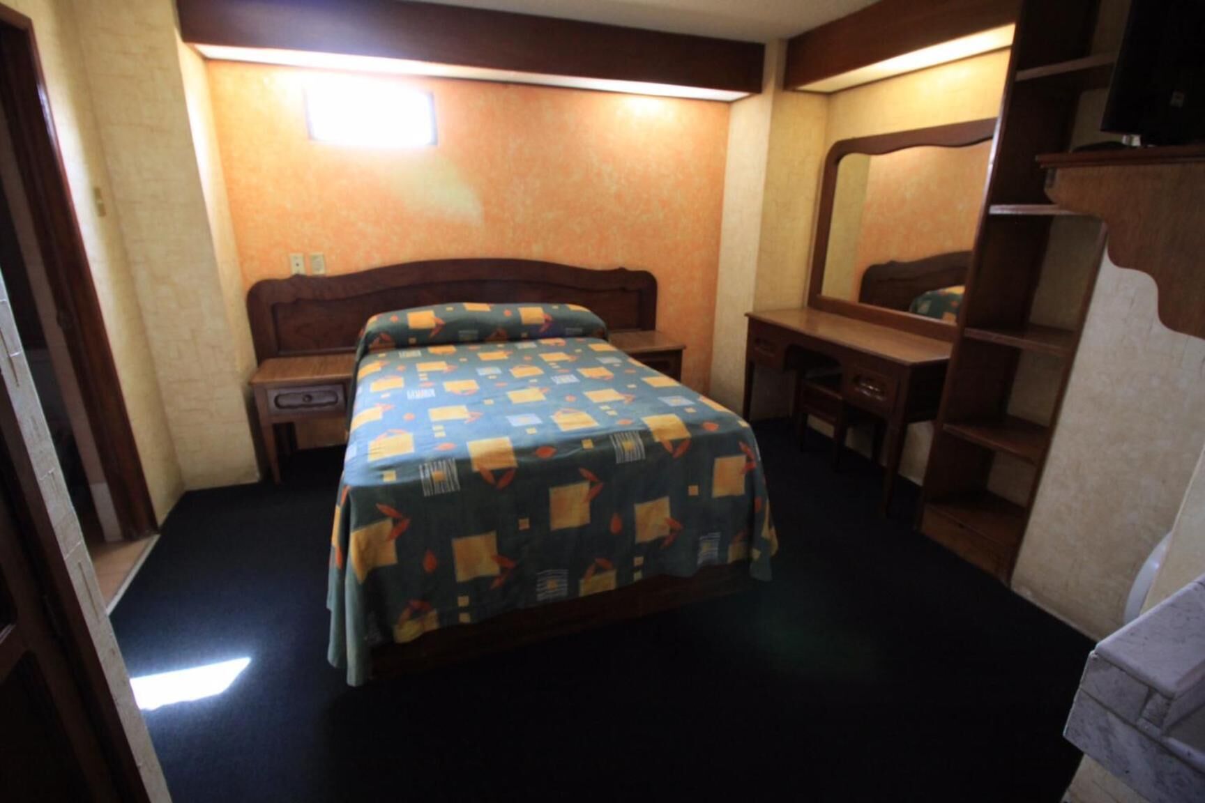 A hotel room with a bed, a desk, a chair, a dresser, and a mirror.
