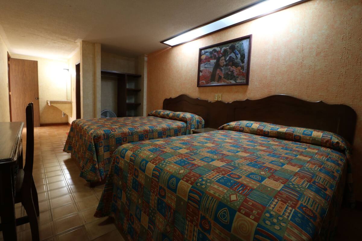 A hotel room with two beds, a wooden headboard, a small table, and a chair.
