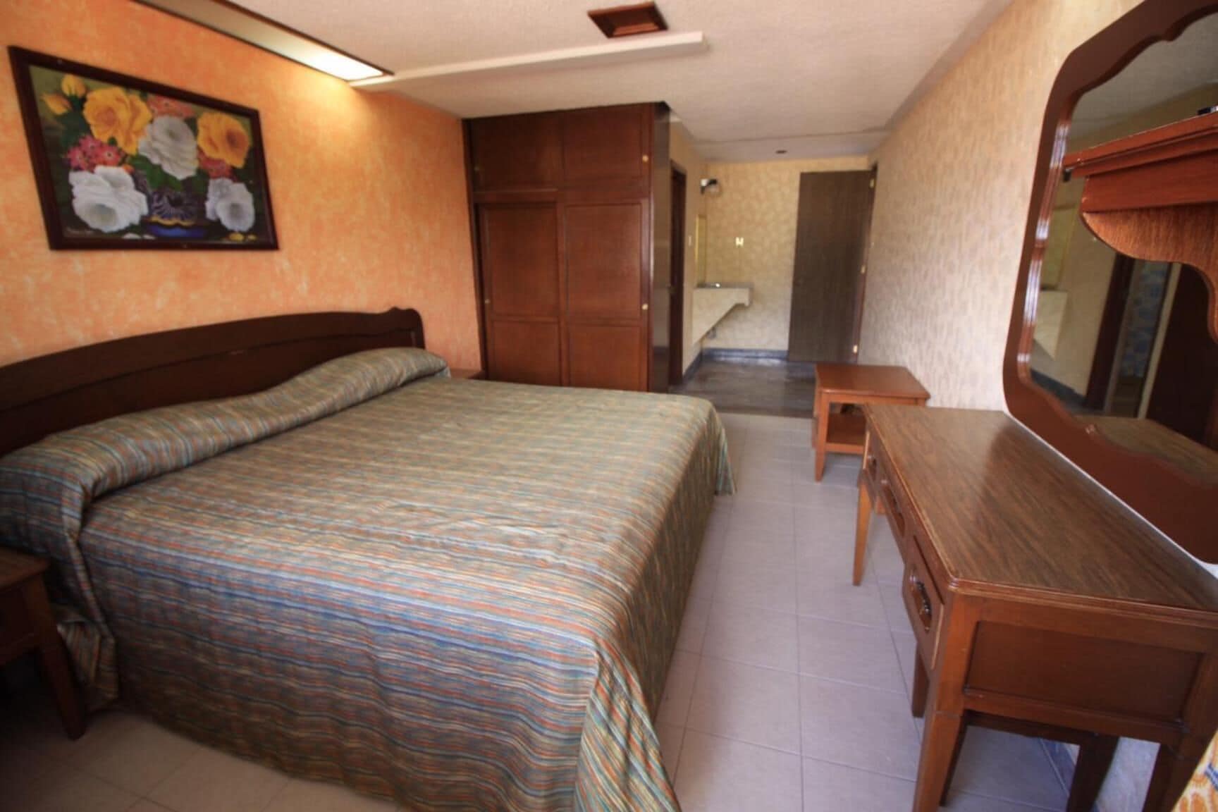 Quarto com cama, cómoda de madeira, mesinha e espelho.