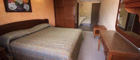 Quarto com cama, cómoda de madeira, mesinha e espelho.