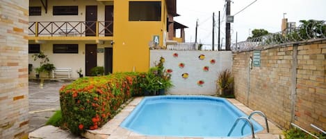 A swimming pool surrounded by a brick wall with a small garden area.