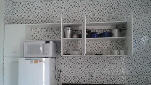 Una cocina con un refrigerador blanco, un microondas y una estufa. Hay armarios sobre la estufa y un salpicadero de azulejos.