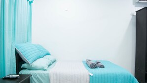A single bed with a teal bedspread, a white quilted blanket, and two pillows. A dark nightstand with a remote control is beside the bed. - Apartamento en PlayaDelCarmen 523 by Sinbad (Playa del Carmen)