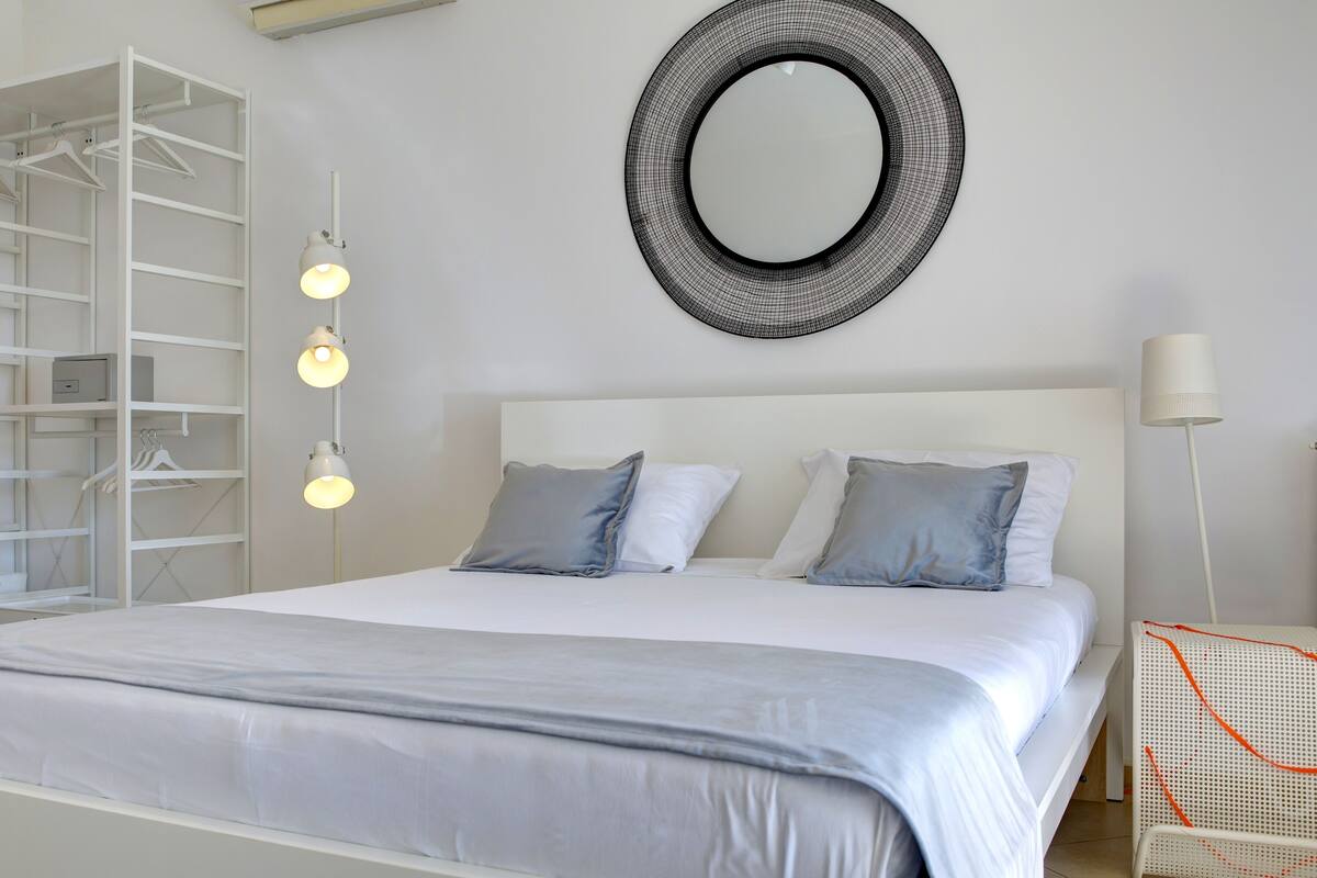 A neatly arranged bedroom with a large bed, a wardrobe, a mirror, and a bedside lamp.