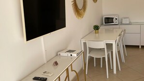 A modern, minimalist room with a flat-screen TV mounted on the wall, a small table with a remote control, a white dining table with chairs, a microwave, and a toaster on the counter. - Villa Katarina 3 (Dubrovnik)