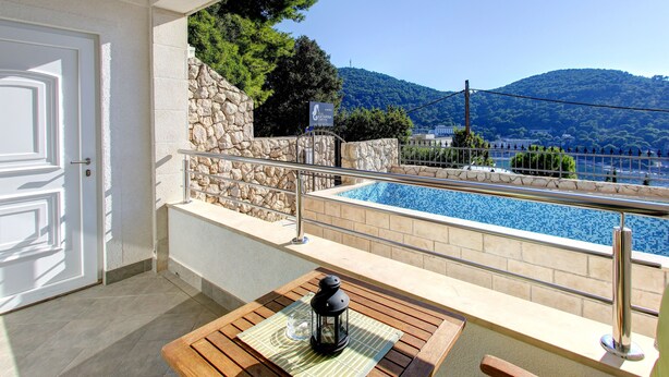 A balcony with a pool, stone wall, and a view of mountains. - Villa Katarina 3 (Dubrovnik)