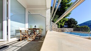 A balcony with a table and chairs, a pool, and a stone wall. - Villa Katarina 3 (Dubrovnik)
