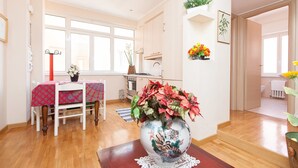 A bright living room with a dining table, a large vase with flowers, and a kitchen in the background. - Rental In Rome Guinizzelli (Rome)