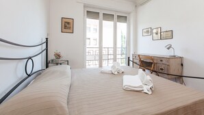 A neatly made bed with towels, a desk with a lamp, and a window with a view of buildings. - Rental In Rome Guinizzelli (Rome)