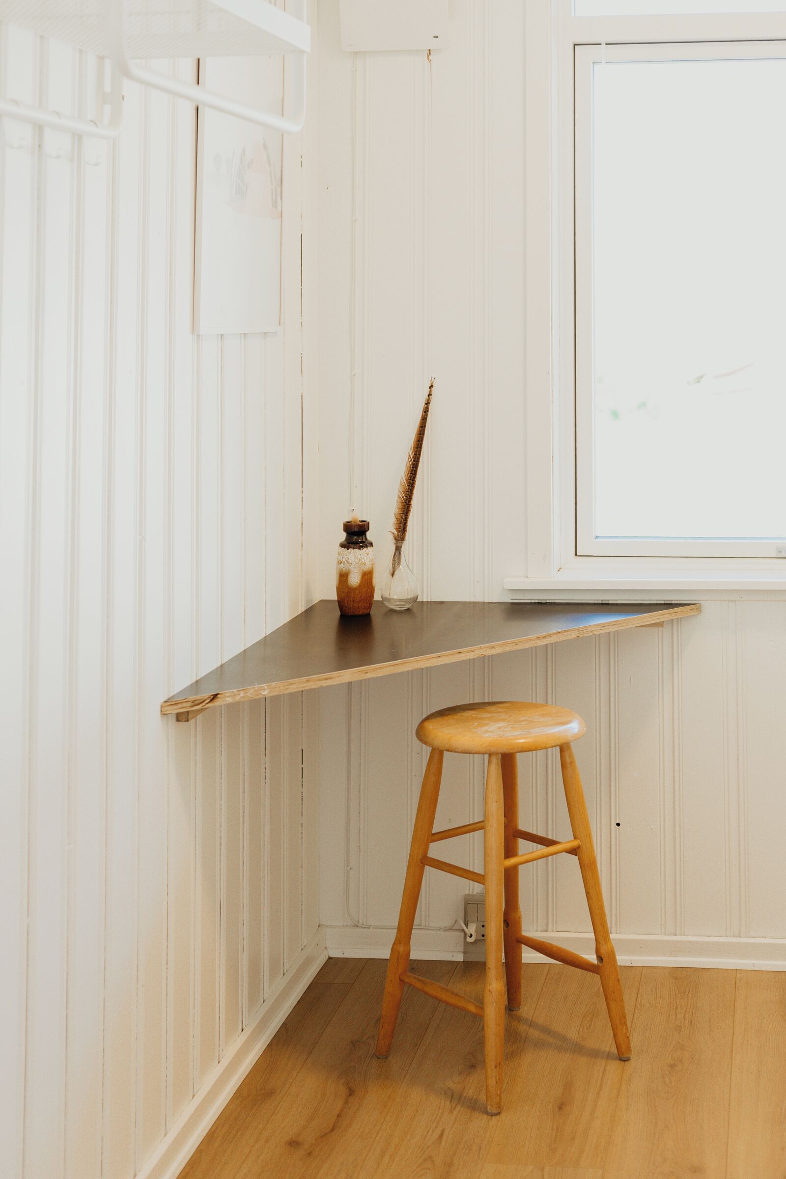A corner of a room with a wooden stool, a small table, and a window.
