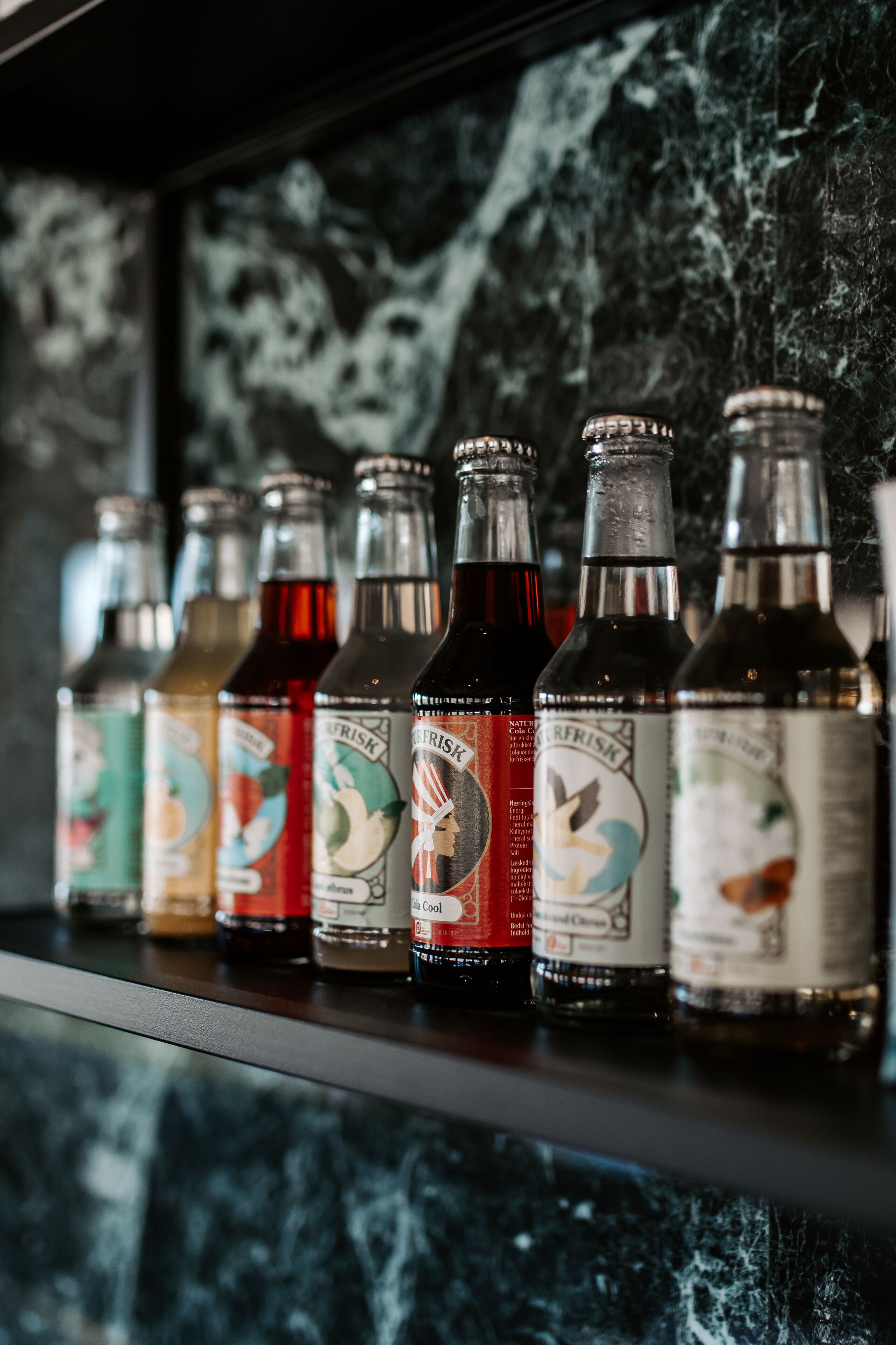 A row of bottles with labels on a shelf against a dark, textured background.
