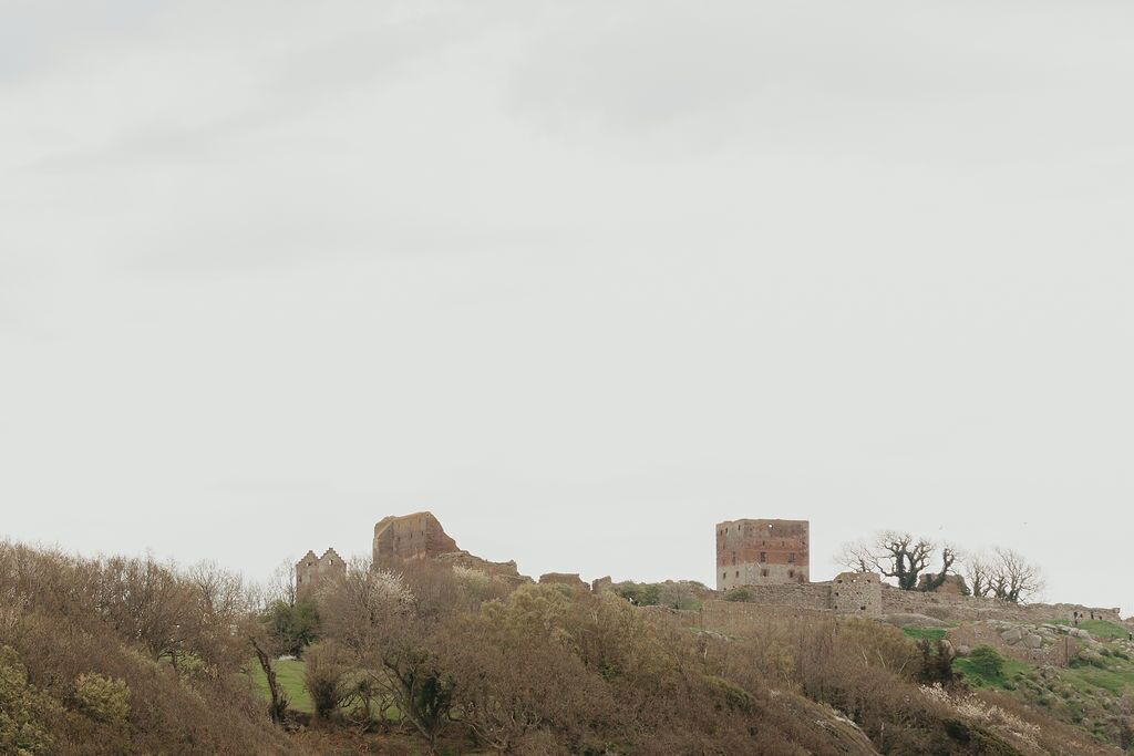 Eine altehrwürdige Steinkastelle mit Ruinen und einem hohen Turm, umgeben von trockener Vegetation und Hügeln.